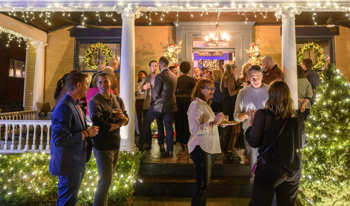 Guests mingling and socializing on the front porch of a festively decorated home during a Christmas celebration.