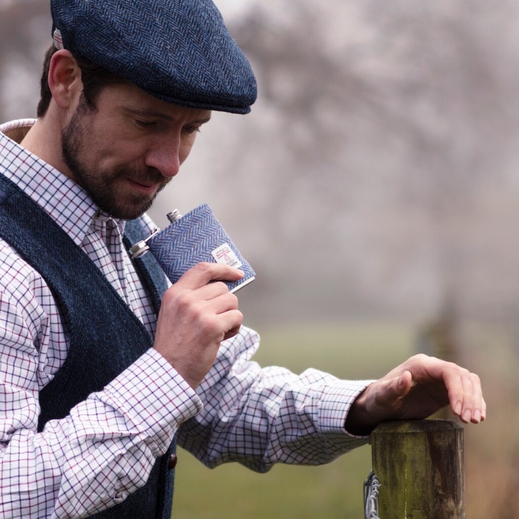A man in a cap drinks from a flask outside.