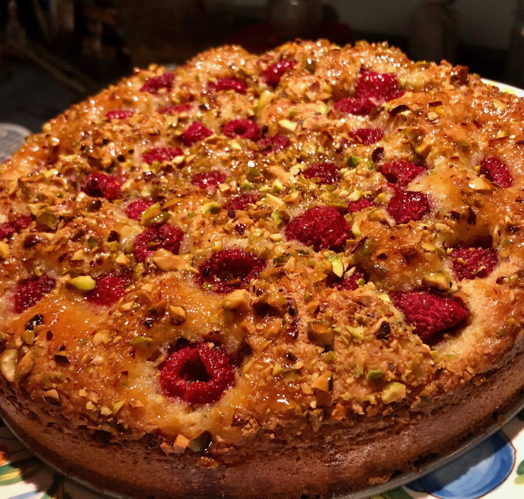 A lemon raspberry Pistachio cake, baked golden brown and topped with fruit