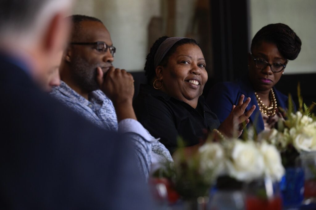 A woman in black smiles at a table full of nonprofit leaders.