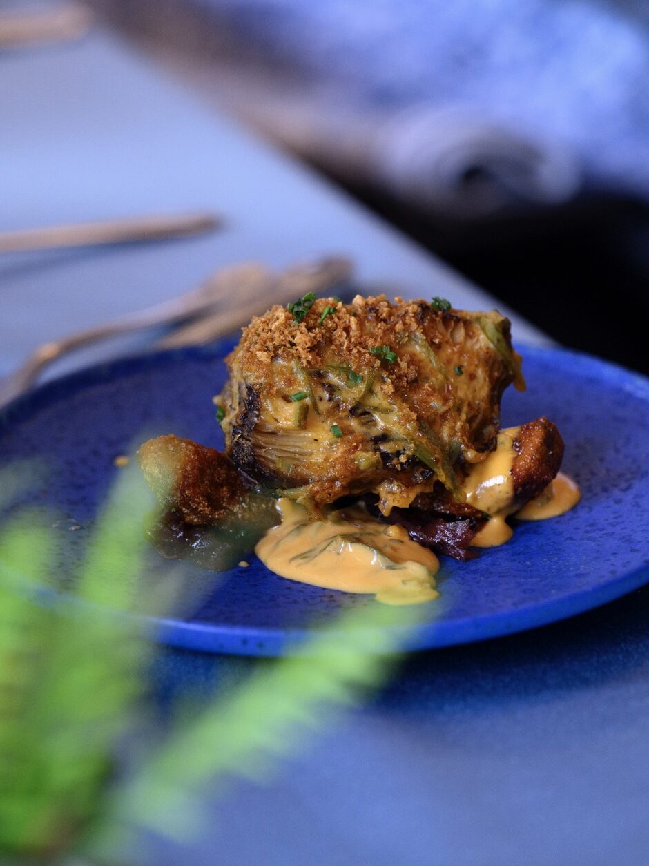 A blue plate with a slice of crumble casserole on it and a bit of grass poking up.