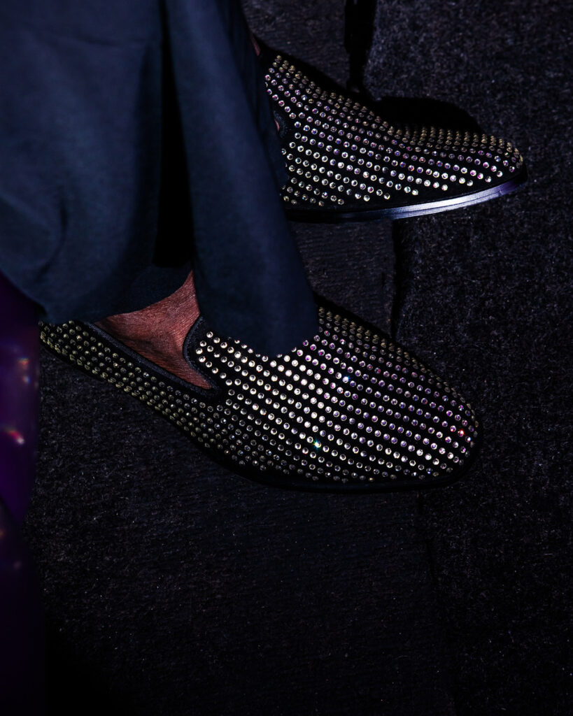 A close-up photograph of a pointed-toe low-heel black slip-on shoe.