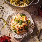 Plate of shrimp ceviche consisting of cooked shrimp, lime juice, diced avocado, sliced red onion and jalapeño pepper.