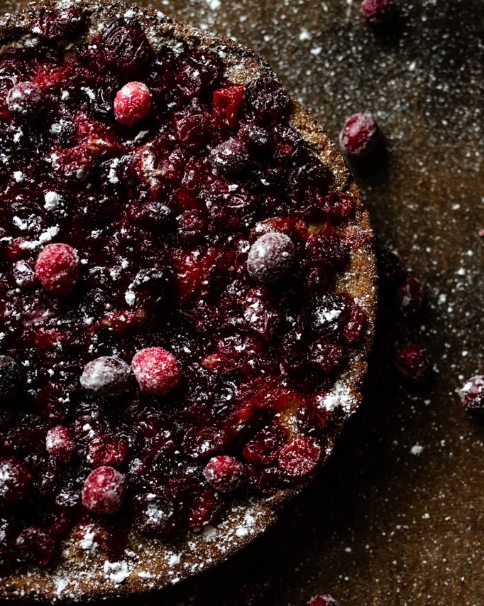 Half a cranberry cake with cranberries and powdered sugar on top.
