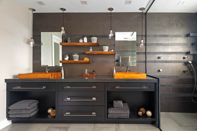 A dark colored double sink vanity with wood accents and pendulum lighting in a bathroom designed by Notion Design.