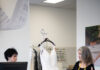 Pittsburgh’s Newest Concept in Bridal Alterations: The Bridal Hub at Warrendale Two women standing on either side of the counter at The Bridal Hub in Warrendale, looking at a white wedding gown on a hanger.