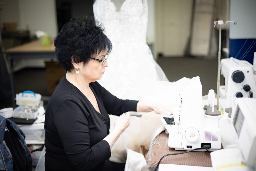 A seamstress at a sewing machine, altering a wedding gown.