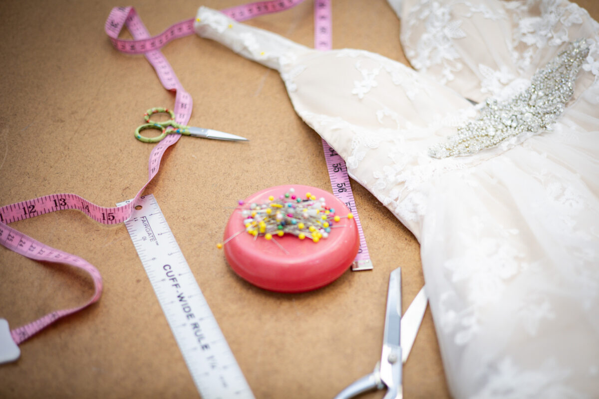 A white wedding dress with alteration tools laying on a table.