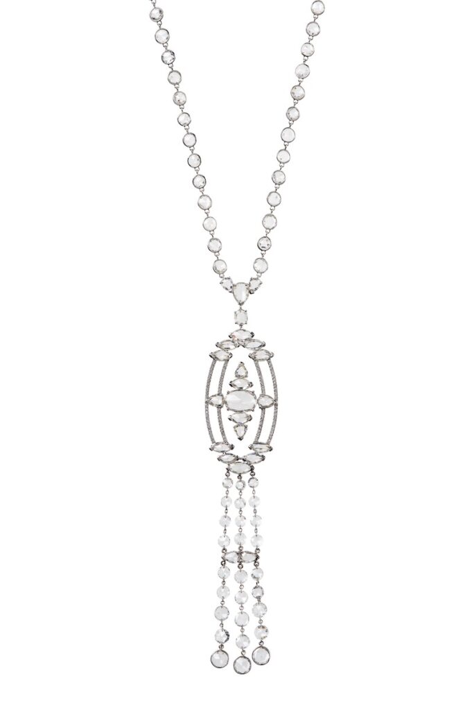 A dainty silver chain necklace with dangles of chains handling from the pendant sits on a white background.