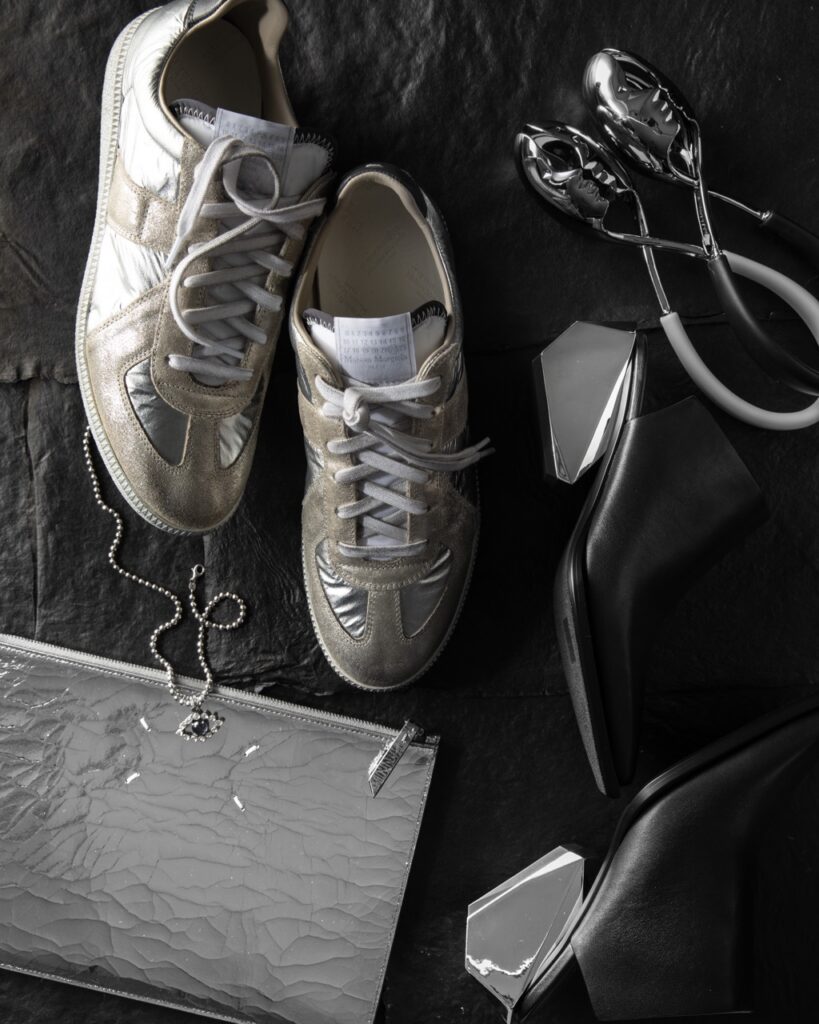 A pair of metallic sneakers amongst a silver bag, silver necklace, and silver shoes.