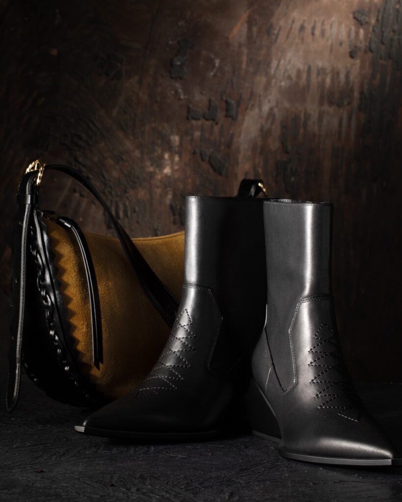 A pair of boots sit in front of a suede bag.