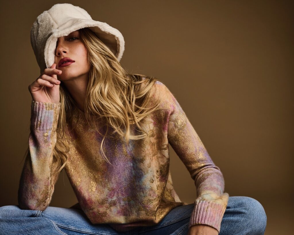 A woman in a gold and metallic long sleeve with a white fuzzy hat on her head.