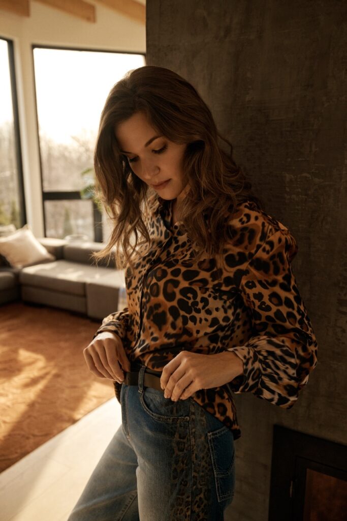 A woman stands in a cheetah print blouse and jeans.