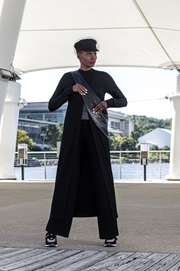 A woman in a long black jacket in a black hat and black bag.