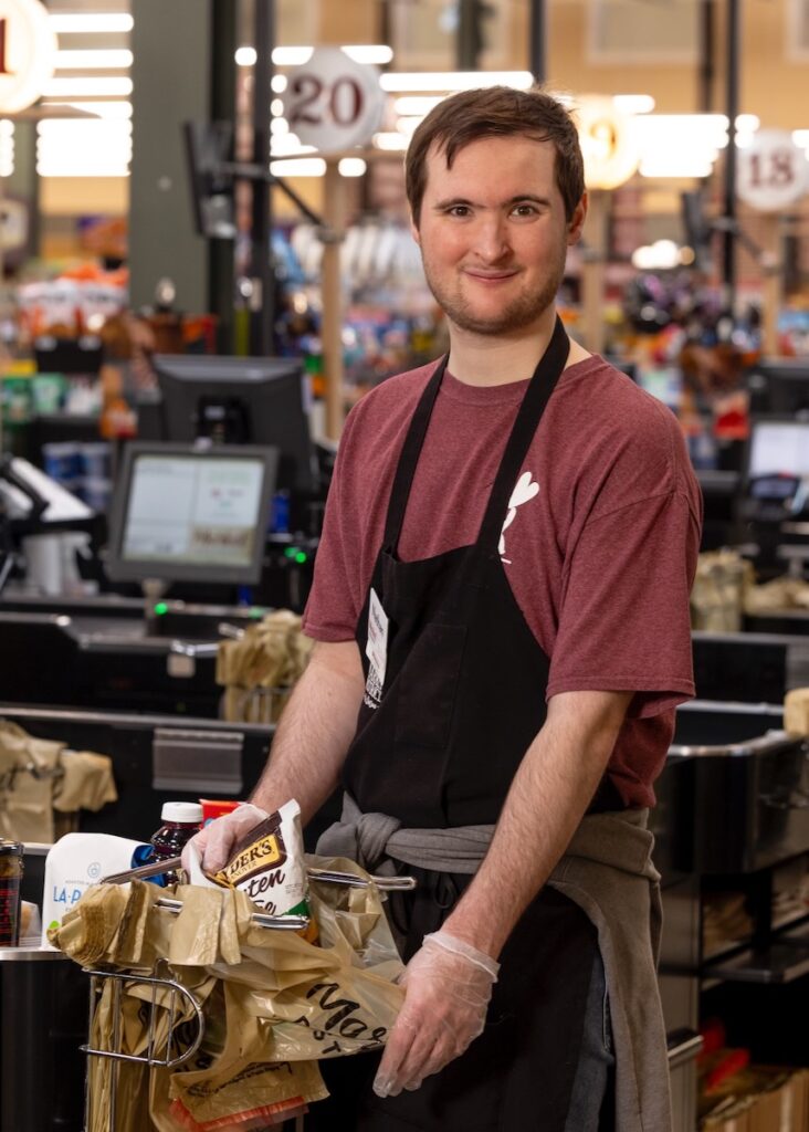 A man in an apron bags groceries.