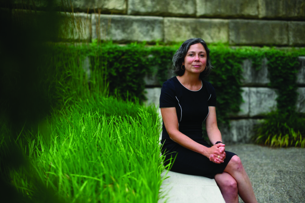 A from ACTION Housing Pittsburgh woman in a black dress sits on a ledge beside a patch of grass.