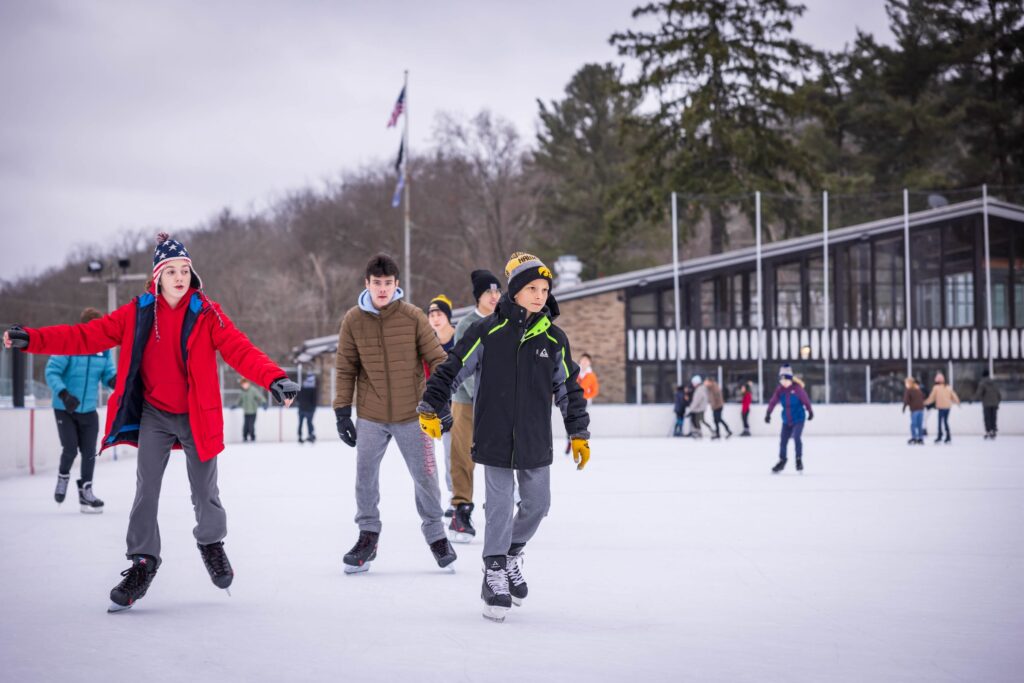 A group on kids in winter coats, skating at an outdoor skating rink at a Pittsburgh park.