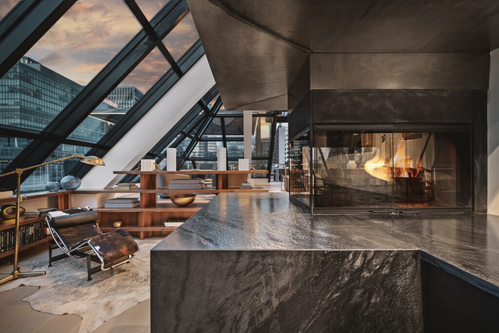 An interior view of the corner of a penthouse with large windows and a black marble fireplace surround from Armina Stone.