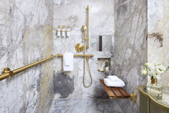 A marble stone shower with gold embellishments and a wood bench. 