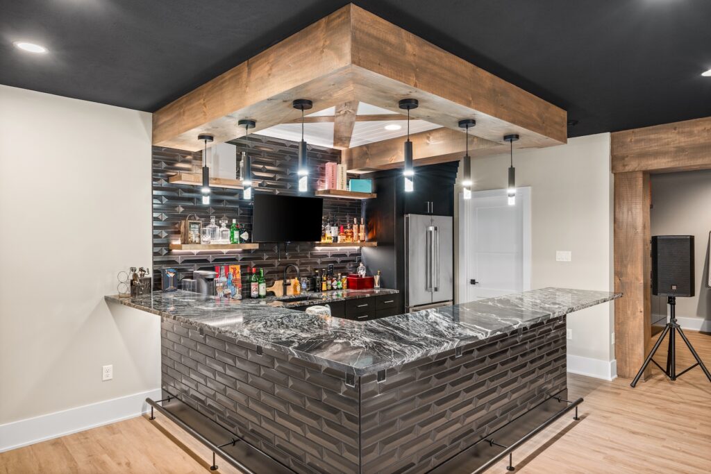 A home bar with dark stone bricks and a marble top with shelves sitting filled behind it.