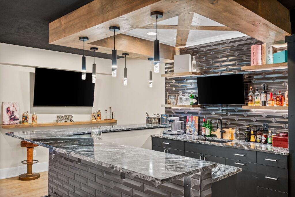 A home bar with black and white marbled countertops by Armina Stone, black cabinets and pendant lighting hanging from wood bulkheads.