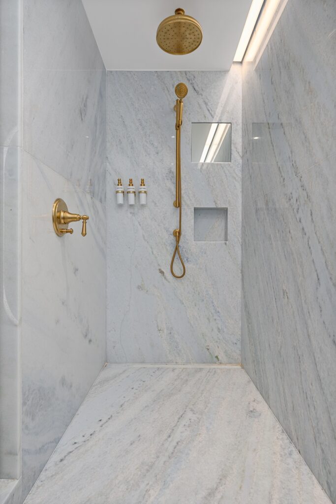 A marble grey shower with gold embellishments on the handle and shower head. 