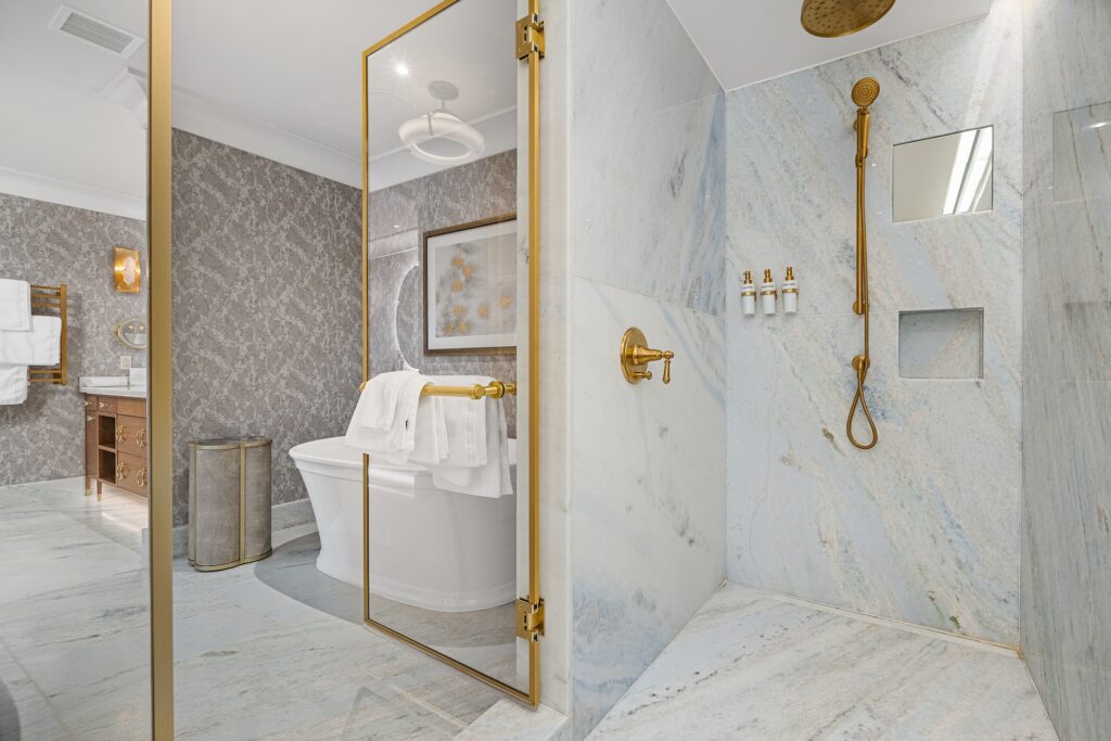 An open shower with stone walls and gold embellishments in a grey bathroom. 