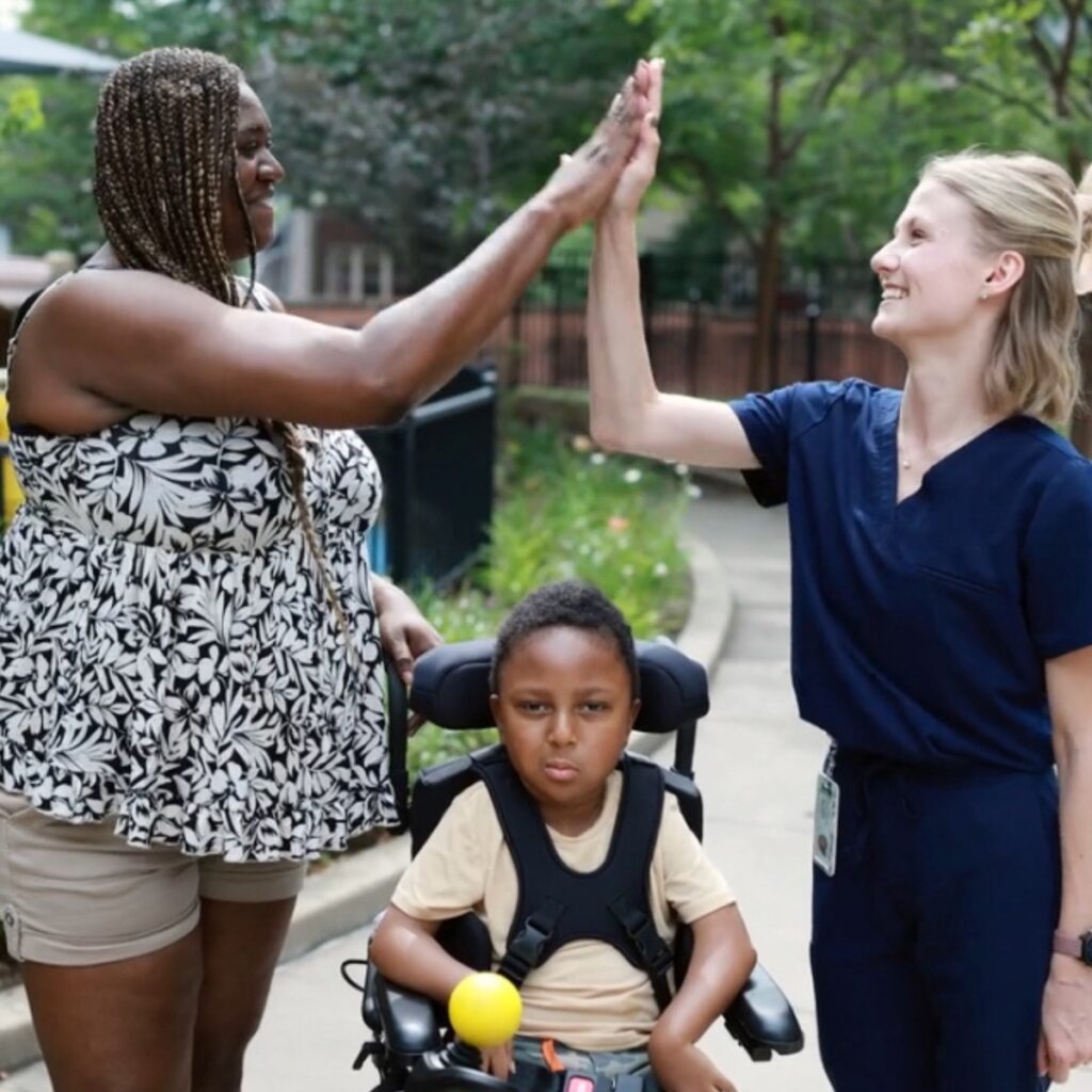 Two women high-five over a child in a wheelchair.
