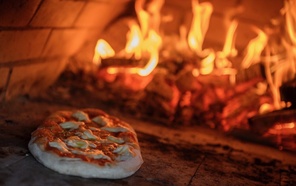 A pizza pie in front of an oven ablaze