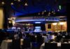 Dining Out for the Win at Rivers Casino An dimly lit, elegant dining space at Rivers Casino with a round bar in the foreground that is highlighted with glowing blue lights.