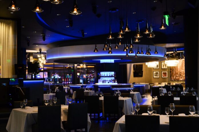 Dining Out for the Win at Rivers Casino 1 - TABLE Magazine An dimly lit, elegant dining space at Rivers Casino with a round bar in the foreground that is highlighted with glowing blue lights.