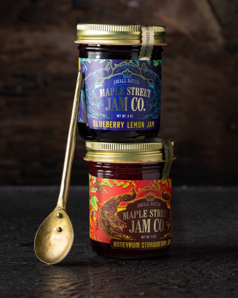 Two jars of jam stacked beside a gold spoon.