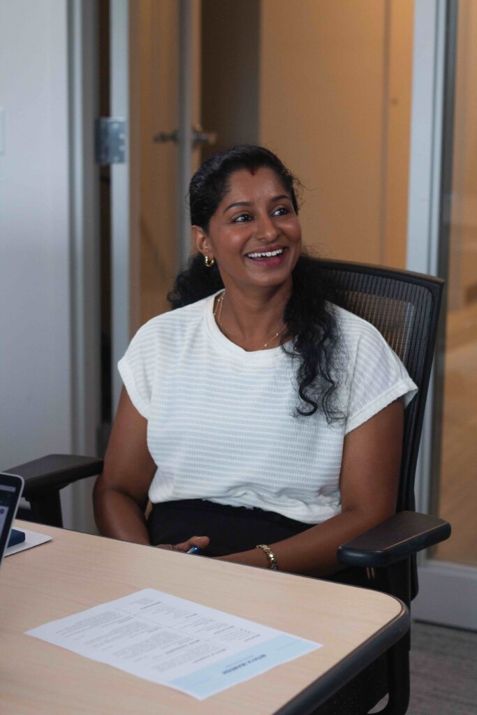 A woman in a white shirt sits at a desk, smiling off to the side of the room.