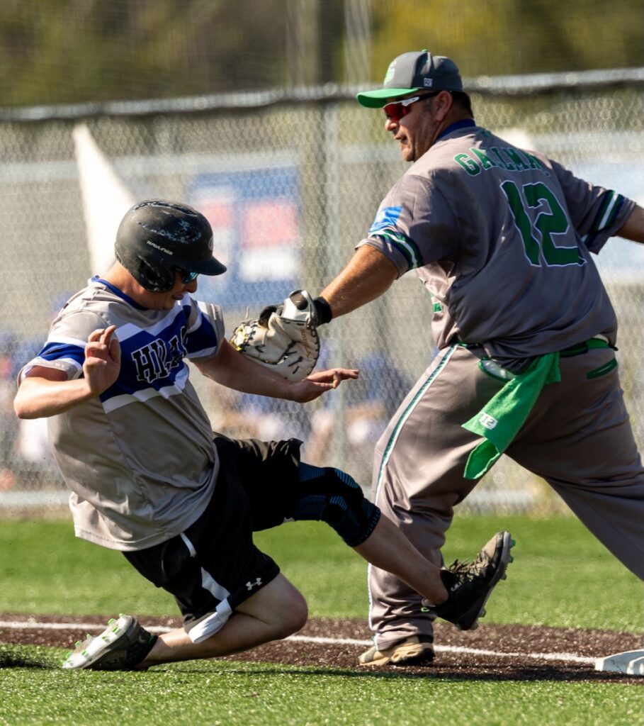 A boy in a baseball uniform slides into a base while another player tries to touch him out.