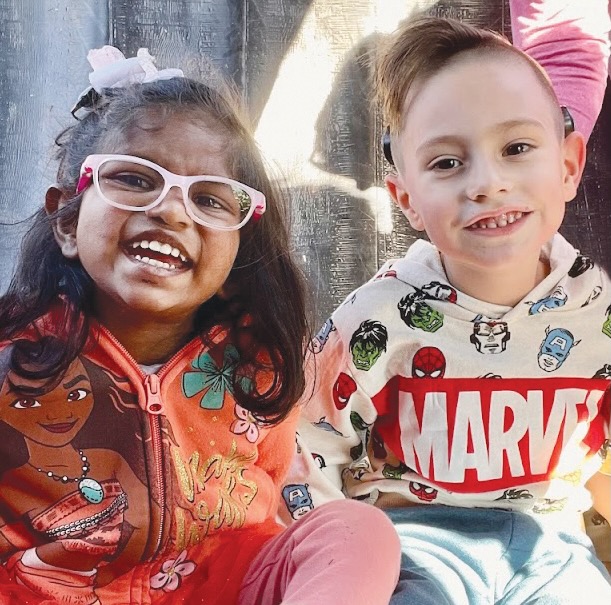 Two children, a girl in a Moana shirt and a boy in a Marvel shirt, sit side by side with smiles.