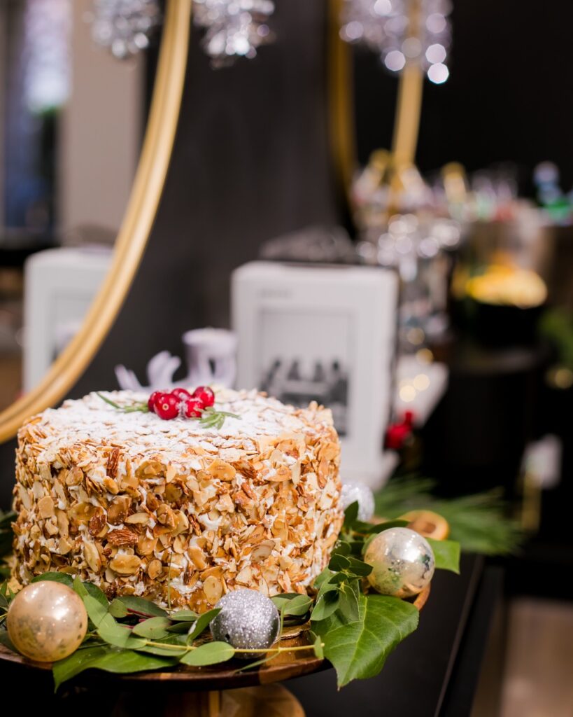 An almond torte cake sits on a black bar with ornaments around them.