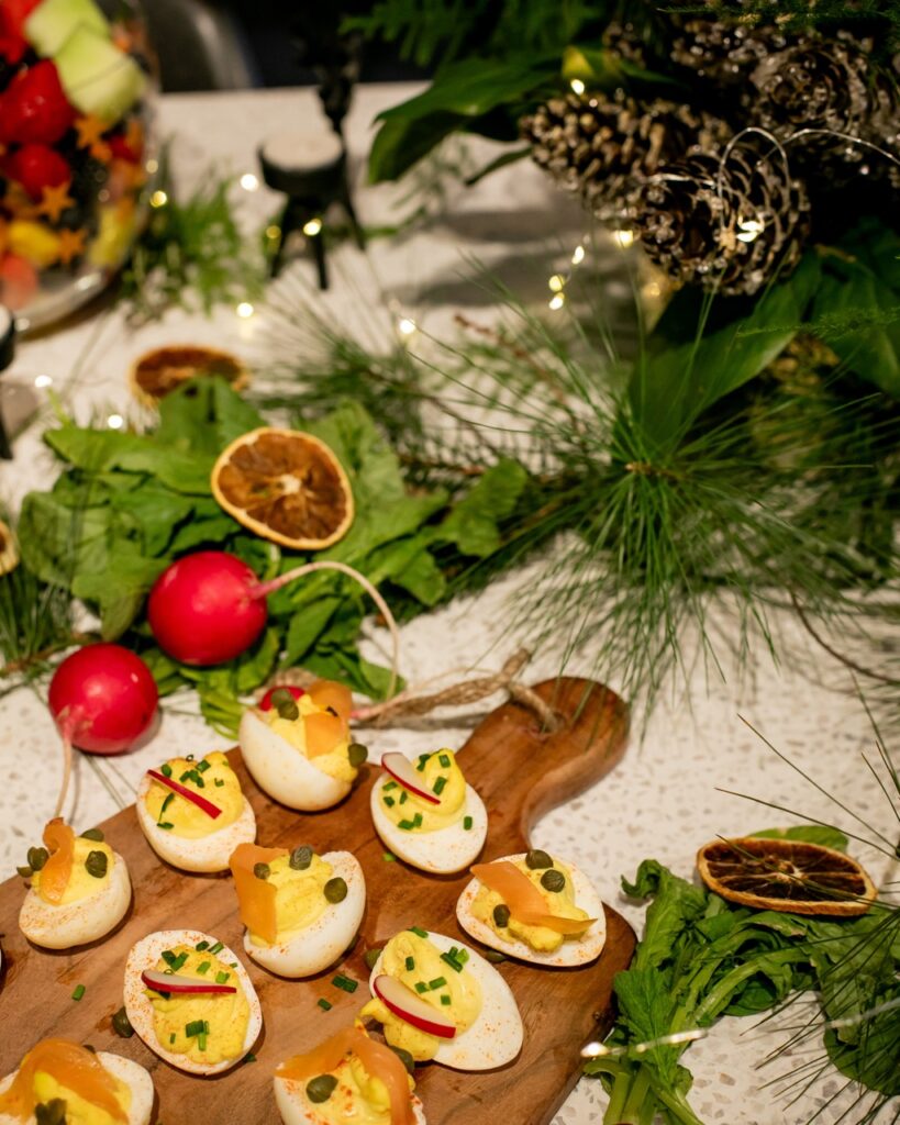 A wooden tray of deviled eggs sit on a white table with greens and citrus slices in the background.