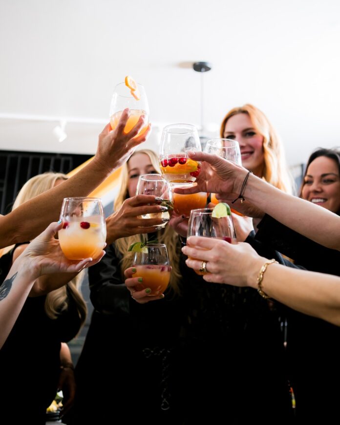 A group of workers at a holiday office party hold their glasses of orange cocktails up to cheers.