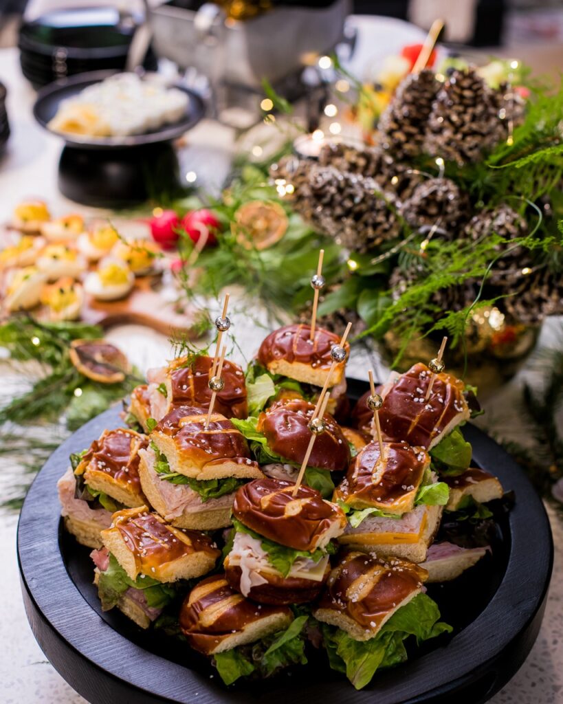 A set of sandwiches on skewers sit on a black platter with deviled eggs and fir trees in the background.