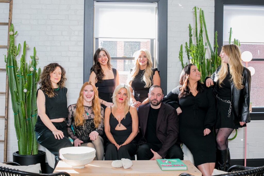 A group of coworkers all dressed in black sit in a white office space.