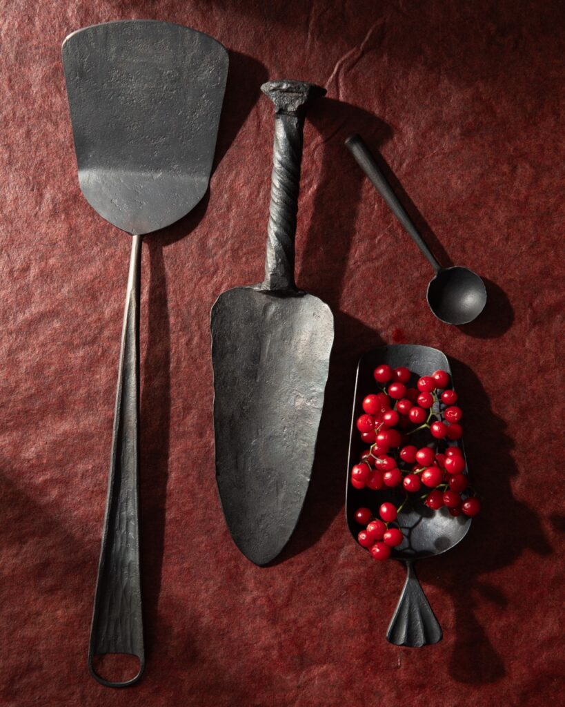 A set of blacksmith made kitchen tools on burgundy paper.