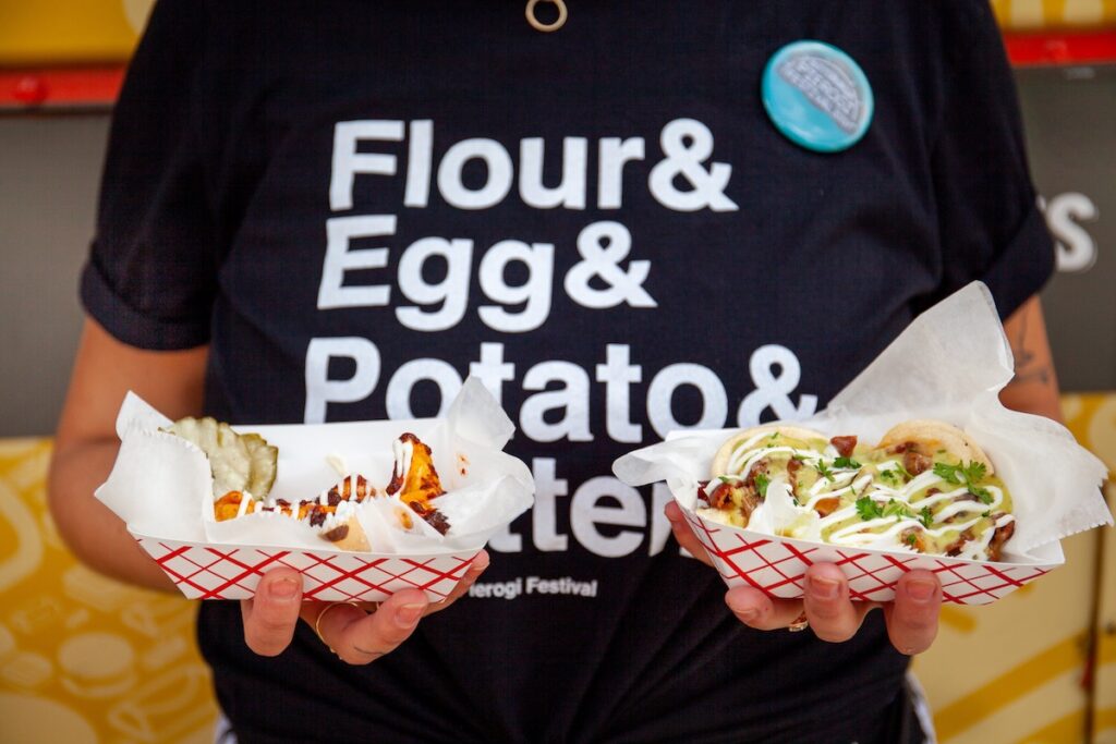 A person in a black t-shirt reading Flours & Egg & Potatoes holds two pierogies