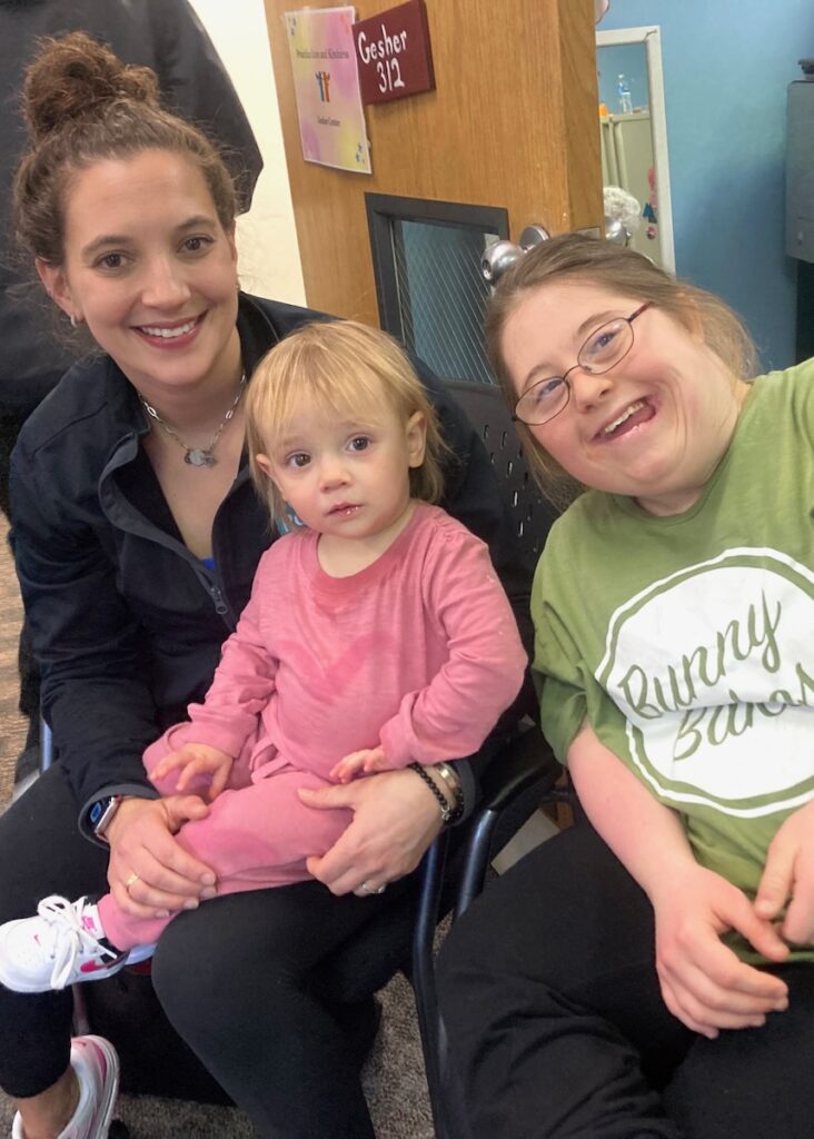 A little girl in pink clothes sits between two women.