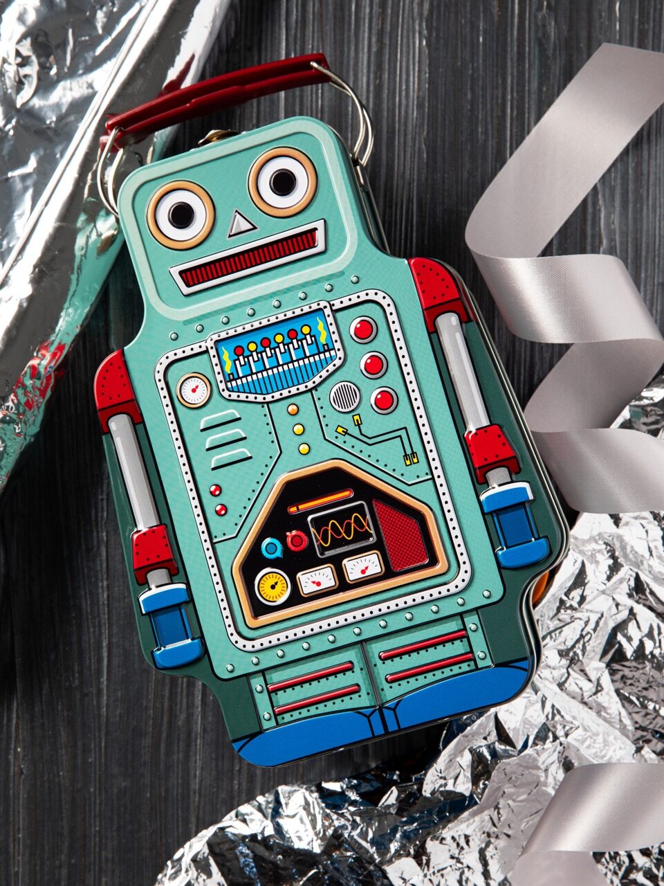 A blue robot kids toy with a handle over the head sits on a black table with silver ribbon and embellishments on the outsides of the photo.