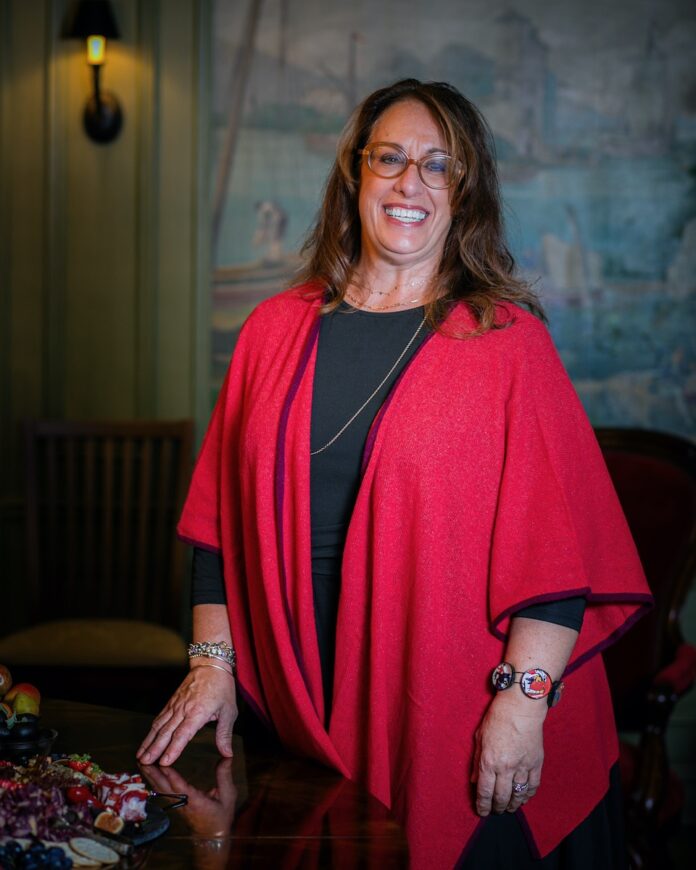 Merrie O'Donnell, a joyful-looking woman in a red shawl, smiles at the camera