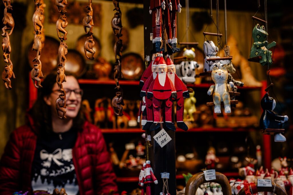 A woman smiles behind various Christmas toys like wooden Santas.