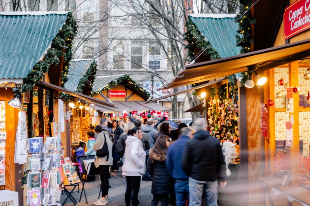 A group of people walk through the wooden holiday market booths in Pittsburgh outside.