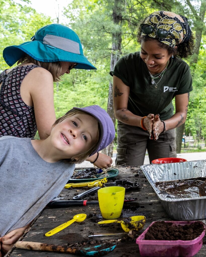A group of kids in hats play in the dirt with various tools.