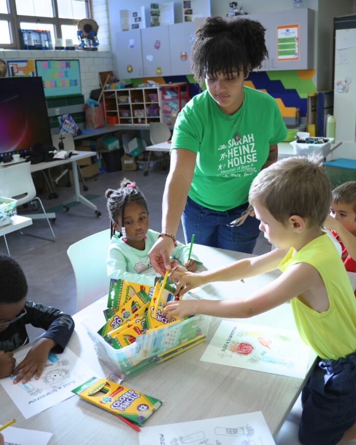 A woman helps kids at a table color.