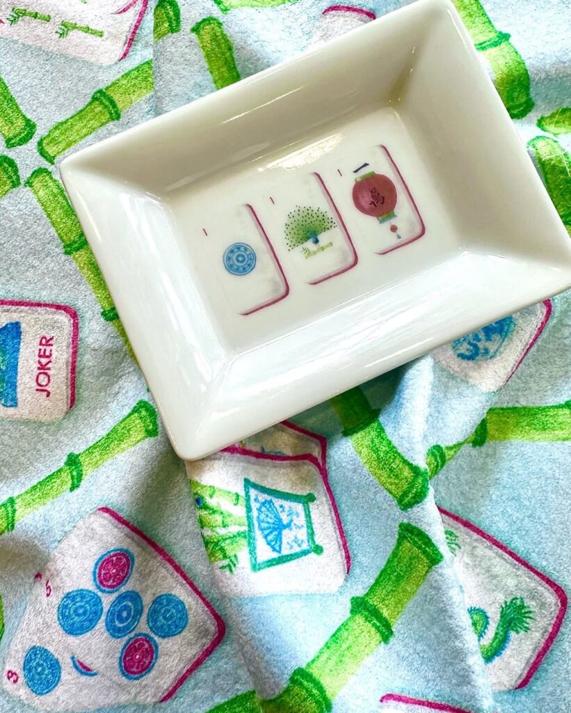 A photo of a fabric with mahjong tiles and an ivory jewelry dish with 3 tiles.
